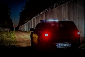 Pojazd SG Pojazd Straży Granicznej nocą, w tle bariera fizyczna na granicy.