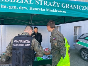 Rywalizacja klas mundurowych w musztrze Stoisko promocyjne Straży Granicznej. Funkcjonariuszka Straży Granicznej oraz dwójka dzieci w mundurach.
