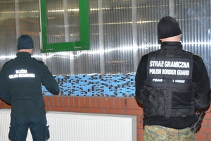 Funkcjonariusze stojący przed papierosami Dwóch funkcjonariuszy przed stosem paczek papierosów