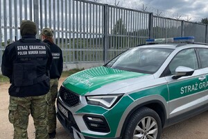 Patrol Straży Granicznej Patrol Straży Granicznej przy pojeździe służbowym, w tle bariera fizyczna.