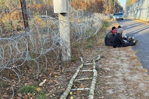 Zatrzymani na pasie drogi granicznej zatrzymani migranci siedzący na pasie drogi granicznej, przy drabinie której użyli do przekroczenia granicy