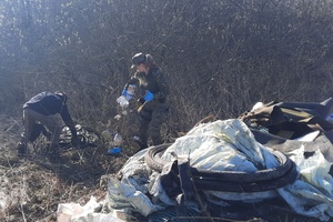 Akcja sprzątania rzeki Biebrzy Dwie osoby sprzątają zarośnięty teren zbierając porozrzucane śmieci. Jedna osoba schyla się, a druga trzyma w rękach plastikowe odpady, mając na sobie rękawice ochronne. Na pierwszym planie widać dużą stertę odpadów między innymi opony, worki i rożne plastikowe przedmioty.