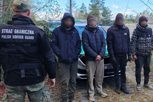 Z Litwy do Polski wbrew przepisom Funkcjonariusz Straży Granicznej stoi z czterema zatrzymanymi po nielegalnym przekroczeniu granicy.