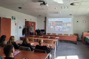 Wspólne szkolenie z Międzynarodową Organizacją do spraw Migracji – IOM Grupa osób siedząca na sali wykładowej obserwuje wyświetlający slajd. Jedna osoba stoi i tłumaczy co jest wyświetlane.