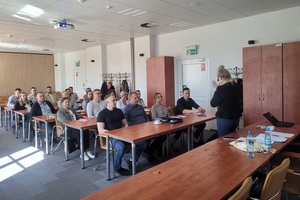 Wspólne szkolenie z Międzynarodową Organizacją do spraw Migracji – IOM Duża grupa osób siedząca na sali słucha wykładowcy, który stoi przed nimi.