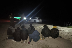 Zatrzymani cudzoziemcy Grupa mężczyzn zatrzymana przez funkcjonariuszy Straży Granicznej siedzi na ziemi.